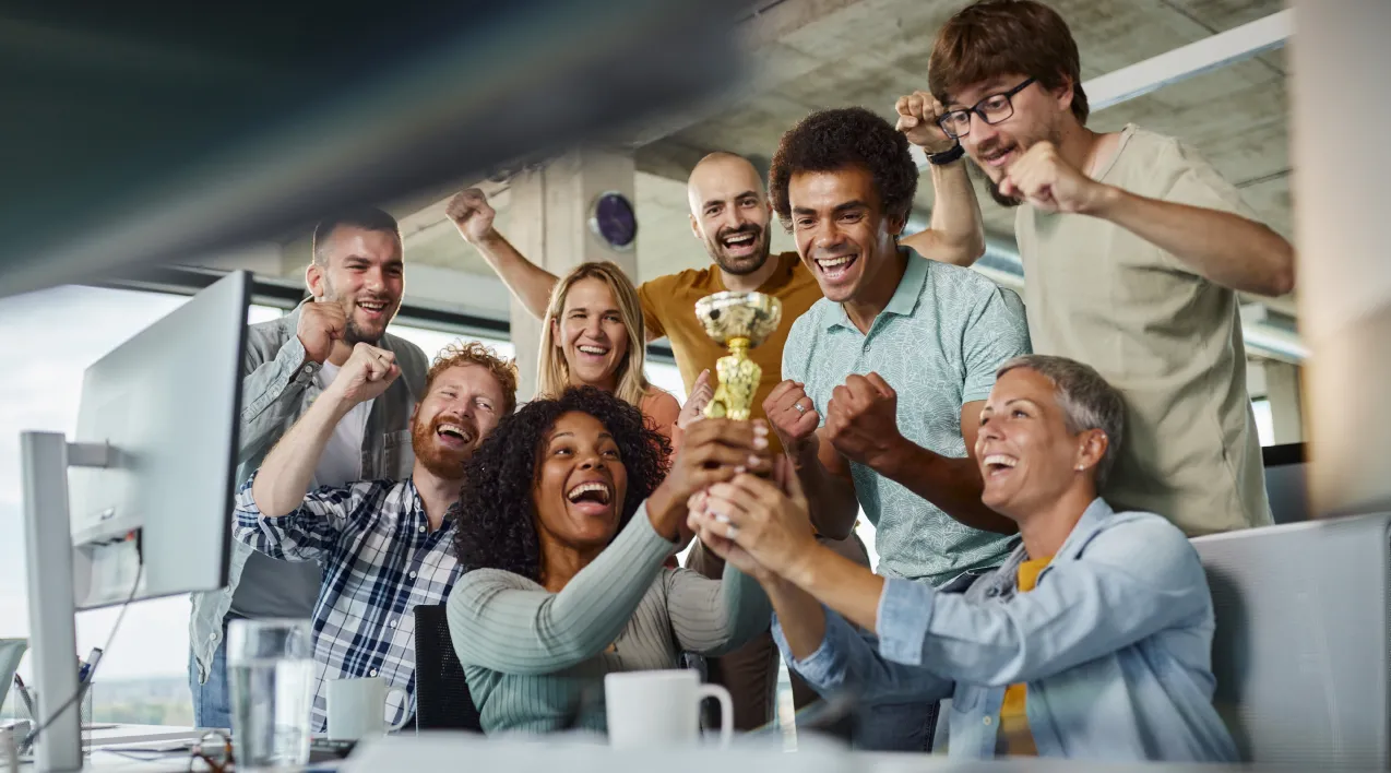 A group of people around a desk cheers while holding a trophy.