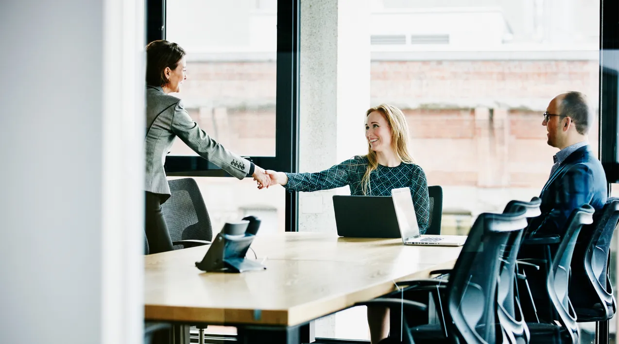 Two colleagues shake hands over a conference table.