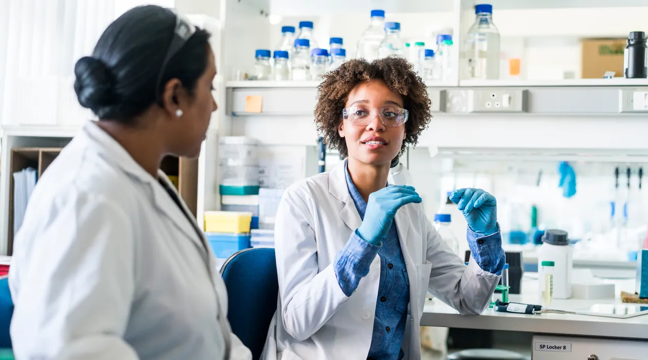 Two women in a lab speak to one another at a counter.