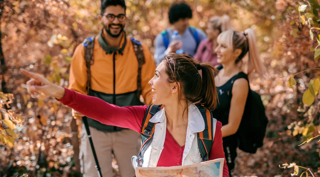 A group of people walk in the woods being led by a woman with a map.