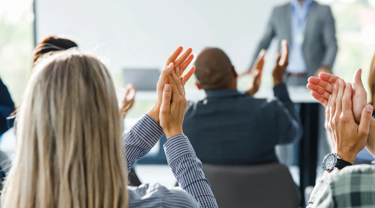 A group applauds a man giving a presentation.