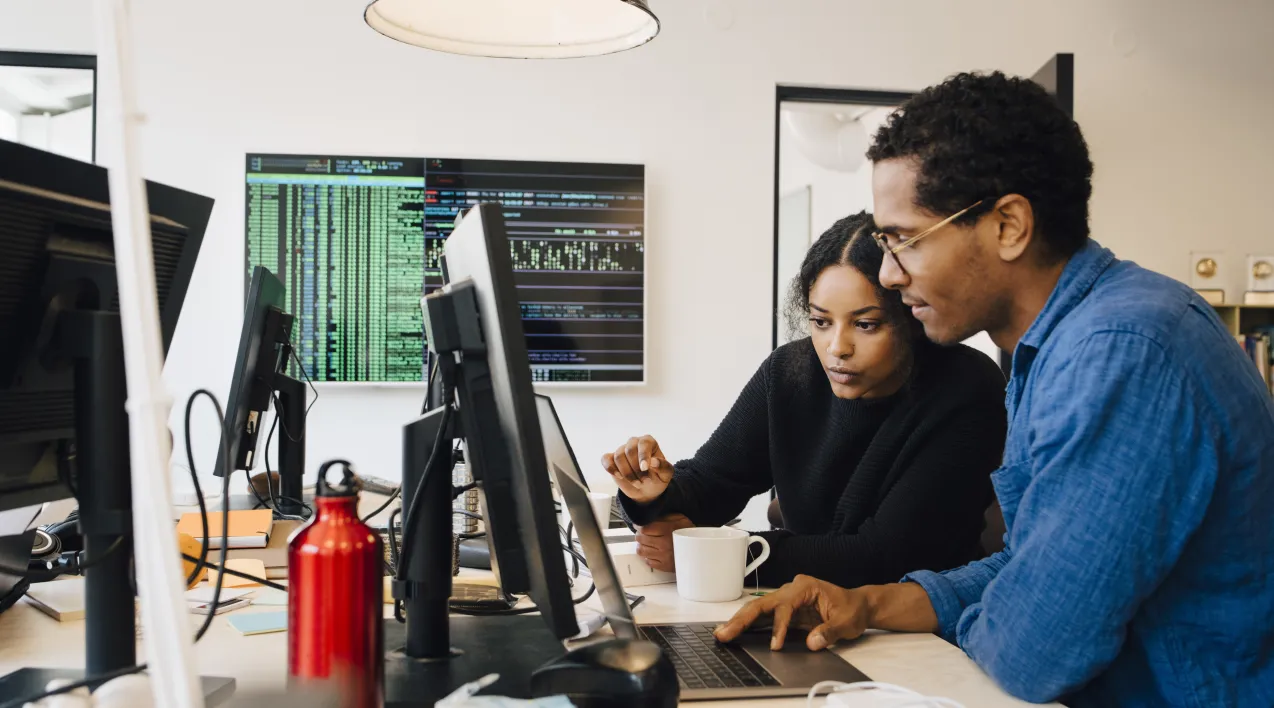 A man and a woman look at a computer together in an office environment