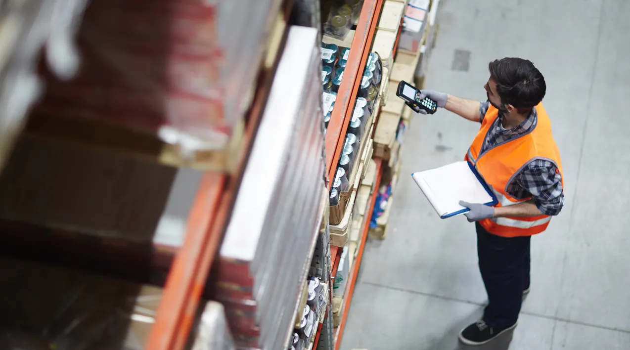 A man working in a warehouse scans product on shelves.