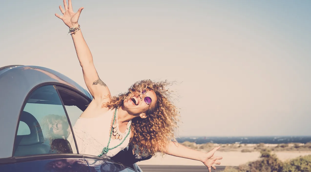 A woman leans out of a car window on a beach.