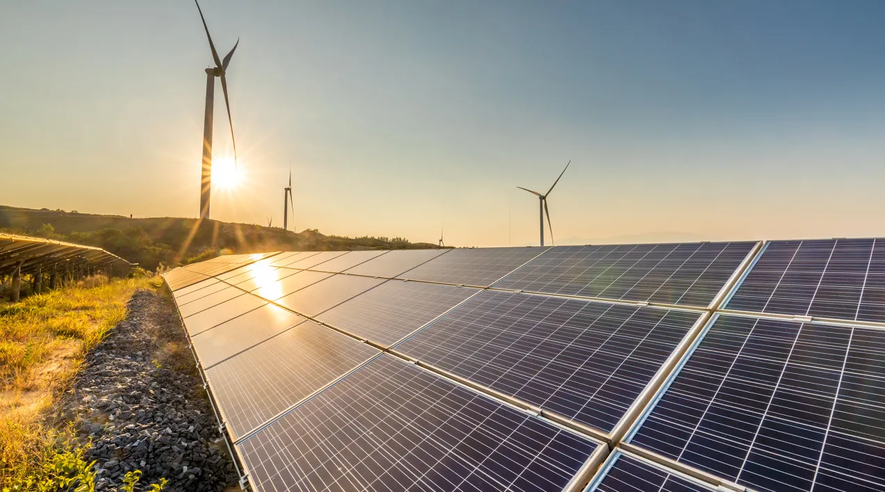 Sunset over a field with solar panels and a wind mill.